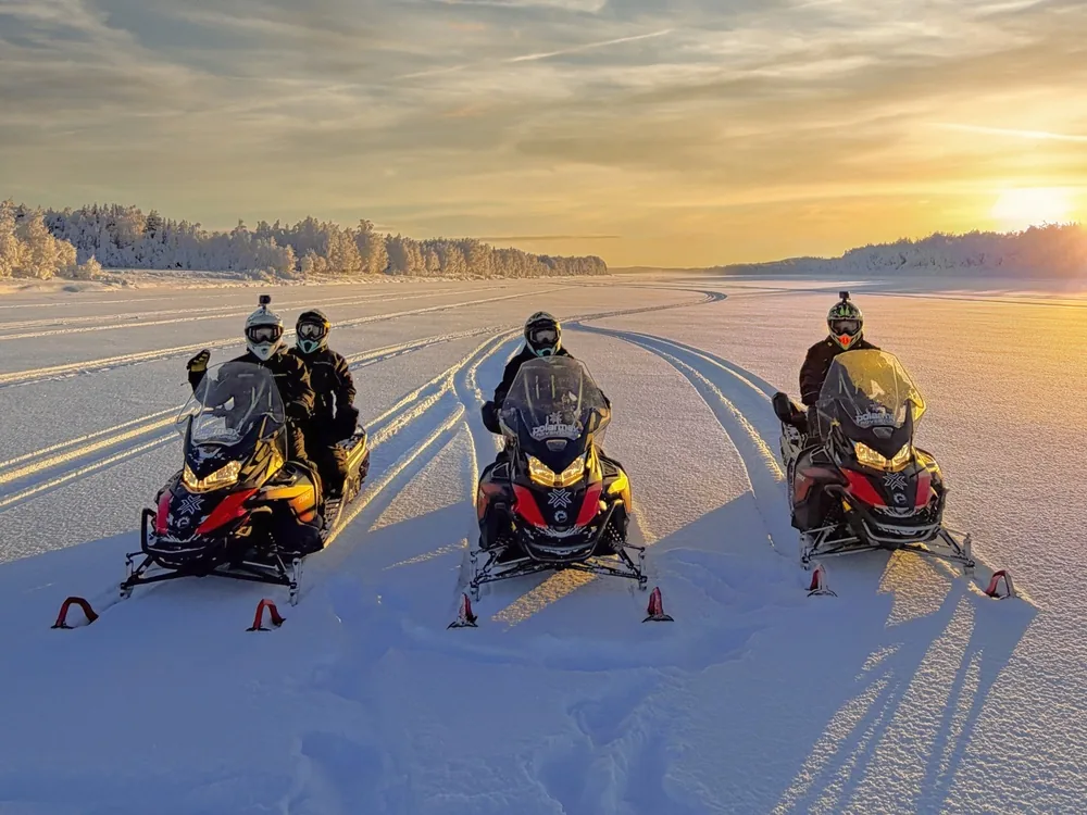 Three snowmobiles crossing a frozen lake at sunset