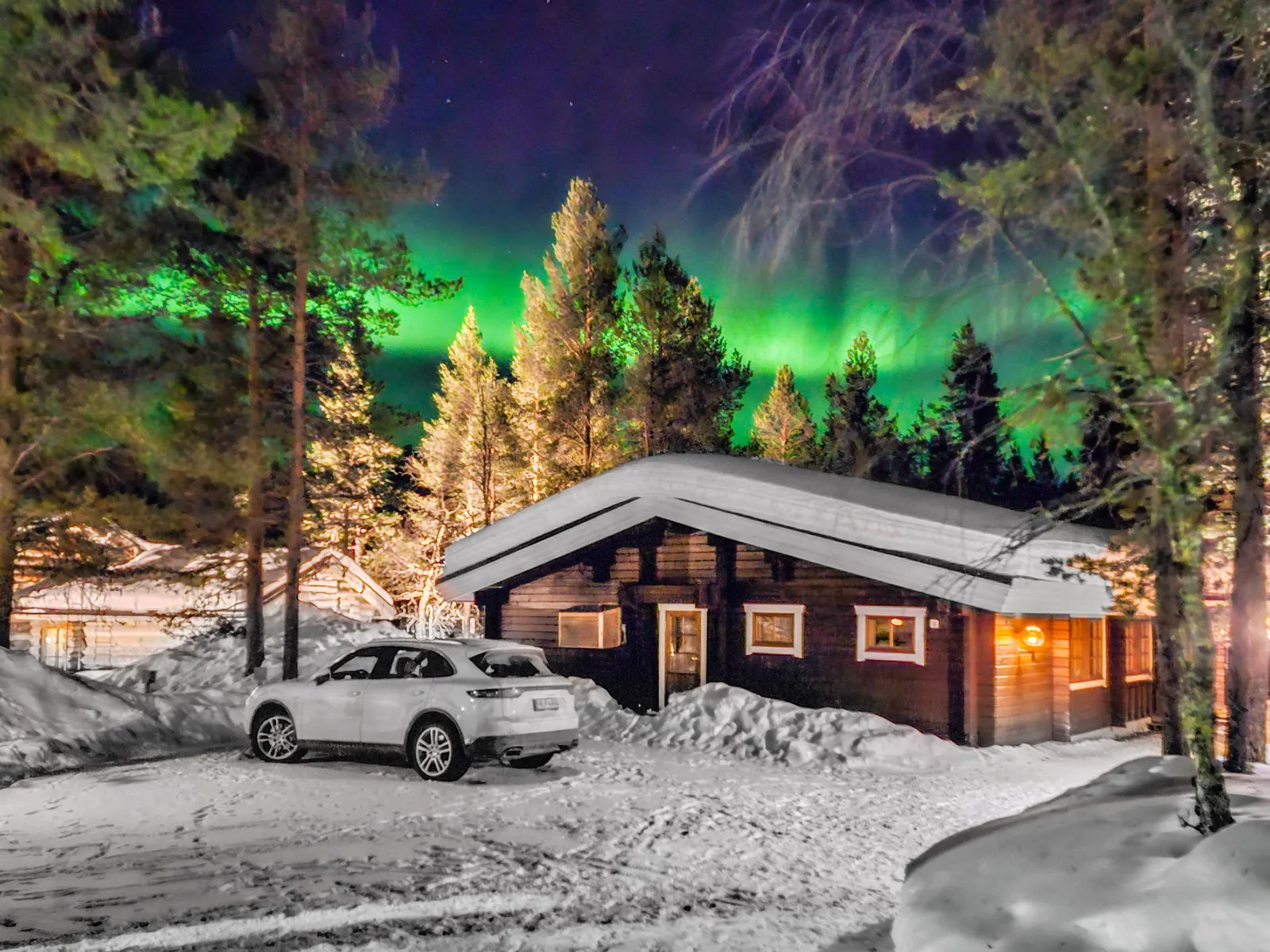 Alkuvilla at night, windows lit, the aurora above the treeline