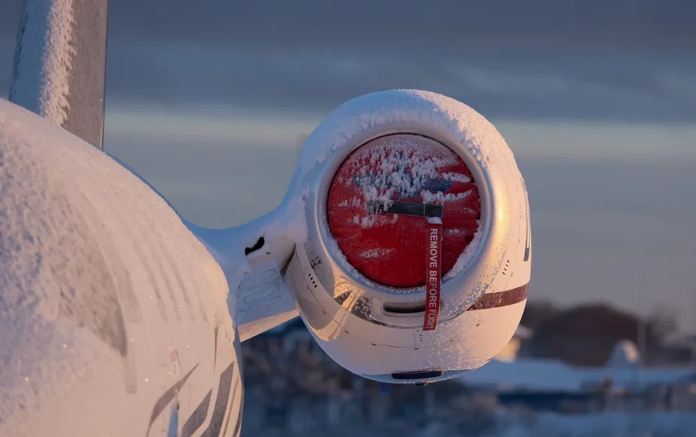 Snow-covered rear-mounted aircraft engine with a red intake cover