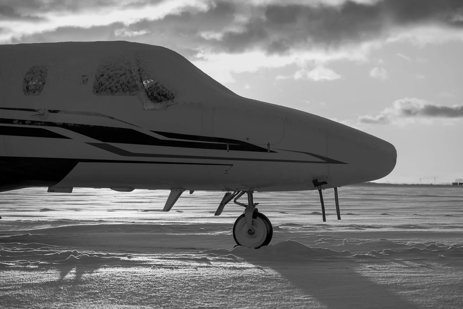 Black-and-white profile of a snow-covered business jet nose on a winter apron