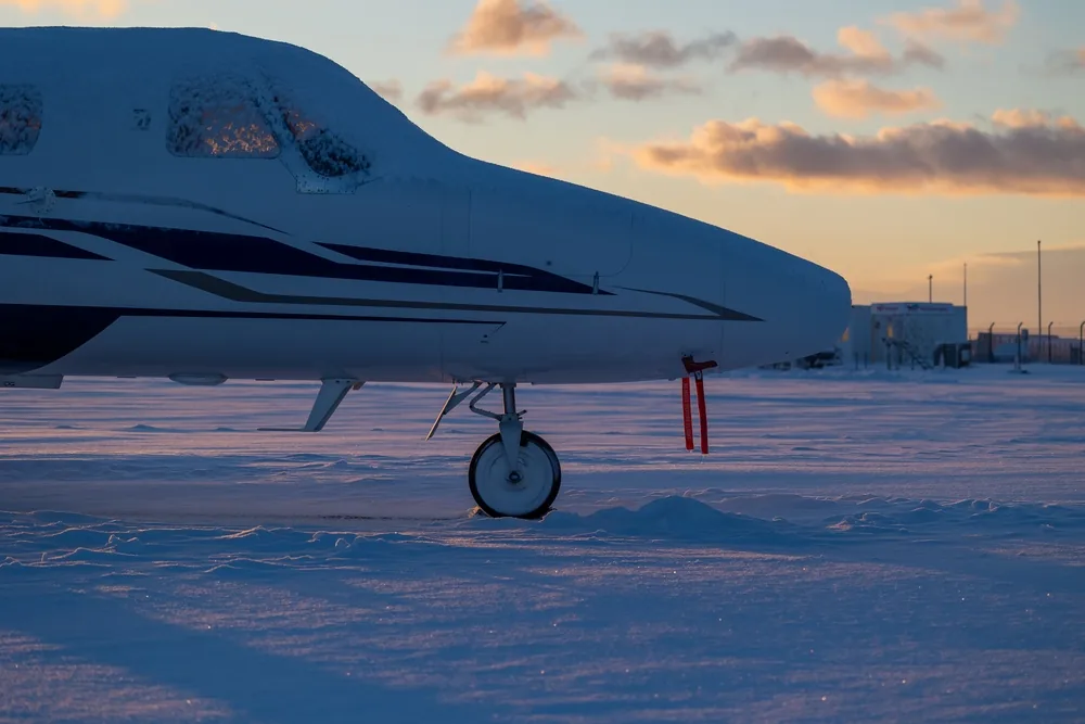 Snow-covered business jet standing on an apron in pink winter sunset light