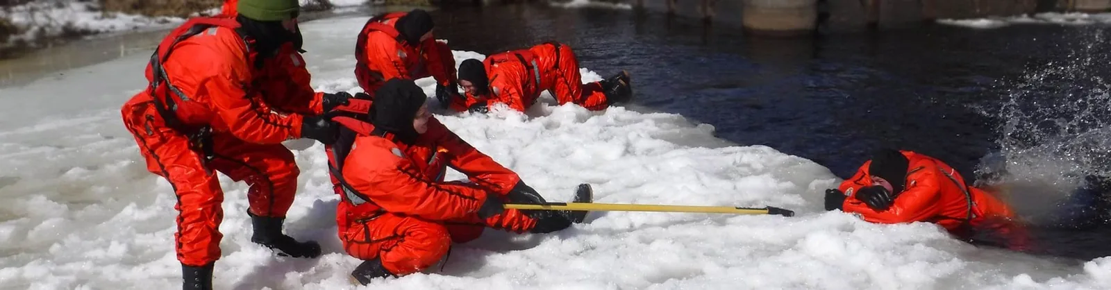 An ice-rescue training team in red drysuits working together on snow and ice