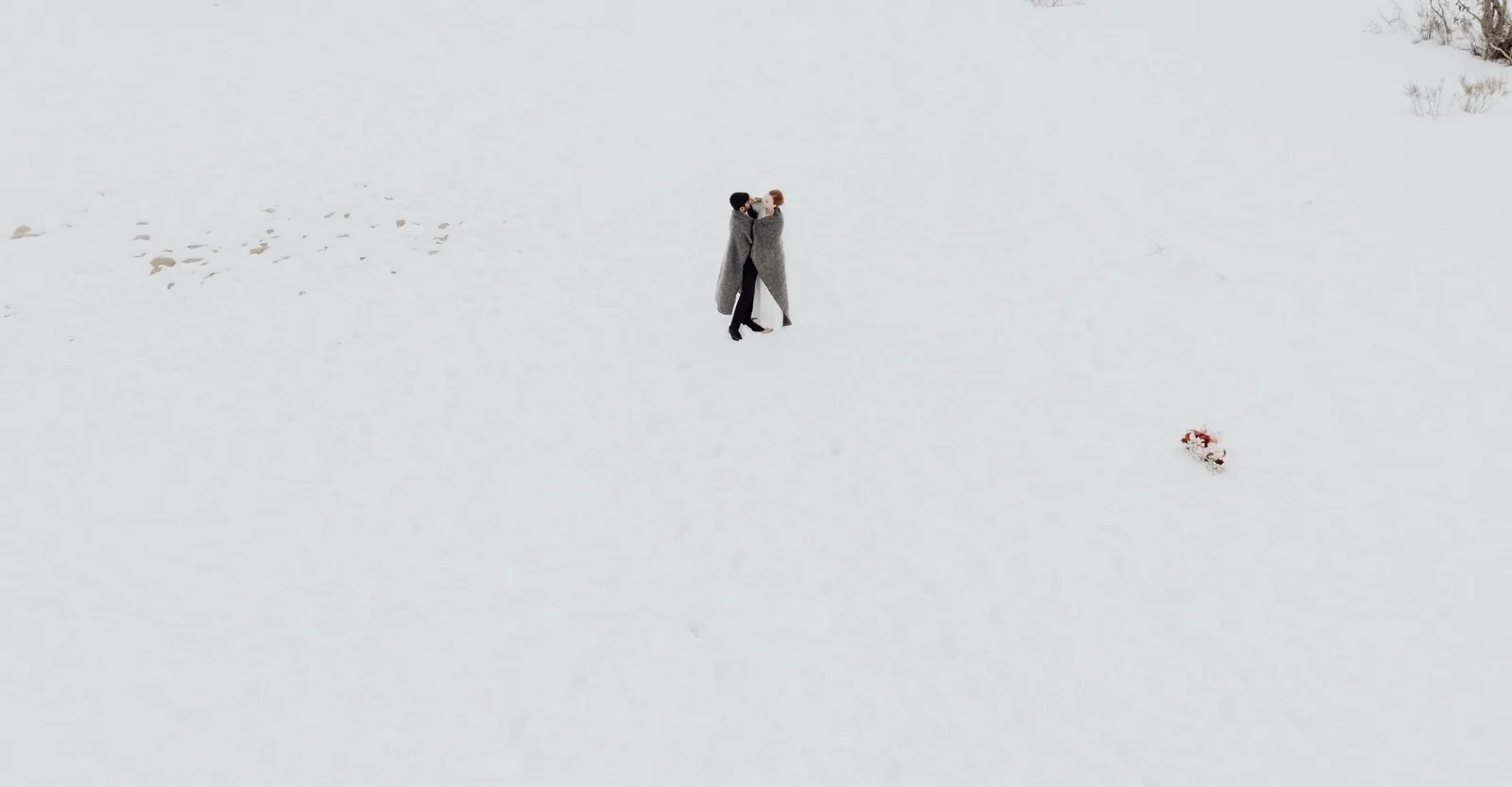 Two small figures wrapped together near the centre of a broad snowfield