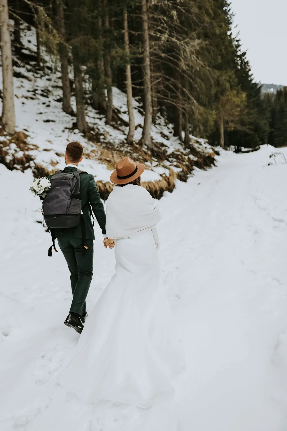 A couple seen from behind walking hand in hand along a snow-covered forest track