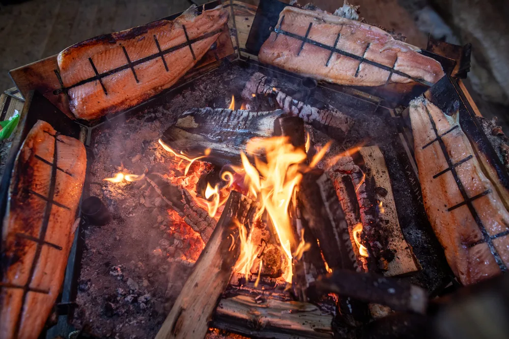 Salmon cooking on a wooden board beside an open fire