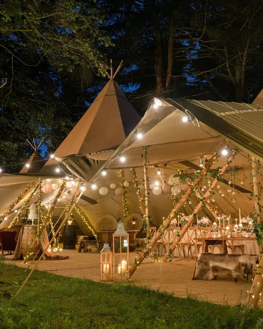 A canvas Tentipi structure lit from within at dusk, with lanterns at the entrance