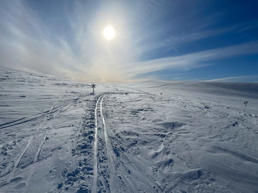 A single track crossing a snowy fell beneath a pale sun halo